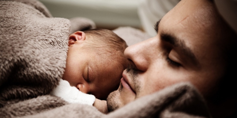 Vater hält mit seinem Baby ein kleines Schläfchen.