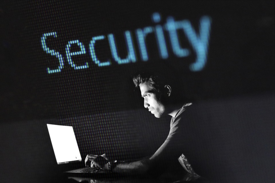 A hacker works on a computer as the word “Security” hangs above him. A hacker works on a computer as the word “Security” hangs above him.